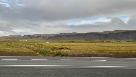 POV-shot-of-cars-on-highway-by-fields-and-mountains-in-cloudy-Iceland