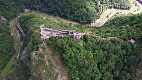 Majestic-aerial-view-of-Poenari-Citadel,-historical-fortress-ruins-on-a-mountain-peak,-surrounded-by-dense-forest