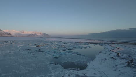 Lago-Aéreo-Y-Congelado-Durante-El-Invierno,-Fascinantes-Montañas-En-El-Fondo-Al-Atardecer