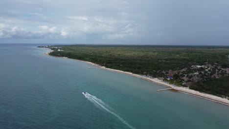 A-boat-speeding-along-the-cozumel-coastline-with-lush-greenery,-aerial-view