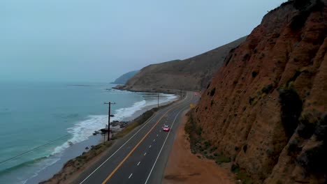 Establishing-drone-shot-as-car-pulls-out-onto-Pacific-Highway-One,-near-Malibu-on-a-grey-and-foggy-morning