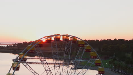 Morning-Sun-Peaks-Through-Seats-Of-Ferris-Wheel,-AERIAL