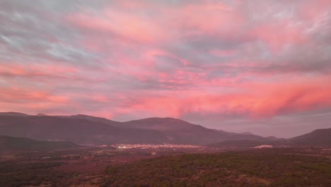 Vuelo-Lateral-De-Drones-Sobre-Un-Valle-Rodeado-De-Montañas-Y-En-El-Que-Hay-Varios-Pueblos-Al-Atardecer-Con-Nubes-De-Color-Naranja-Rosado-Y-Violeta-En-Ávila,-España