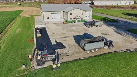 A-crew-paves-a-new-driveway-by-a-rural-homestead-as-the-sun-dips-low,-casting-warm-hues-over-the-tranquil-scene