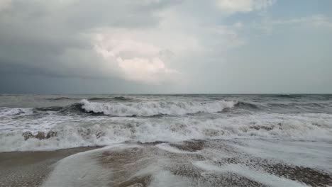 Slow-Motion-Dolly-Backwards-of-Waves-Crashing-onto-Beach,-Overcast-Day