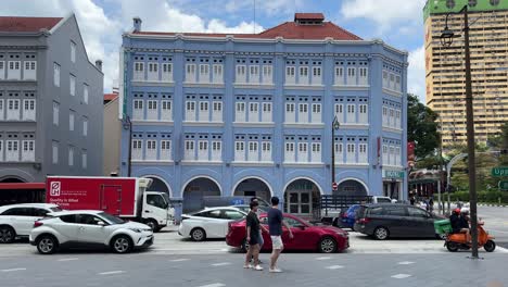 Gente-Caminando-Y-Vehículos-Deteniéndose-En-El-Tráfico-Con-El-Telón-De-Fondo-Del-Hotel-81-Chinatown,-Que-Alberga-Alojamiento-En-Un-Edificio-Patrimonial-En-Medio-Del-Ajetreo-Y-El-Bullicio-De-Singapur.