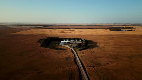 Aerial-Drone-Out-Blue-Sky-Over-Small-Enclosed-Farm-Home-in-the-Middle-of-Vast-Harvest-Blooming-Canadian-Agriculture-Farmland-Fields