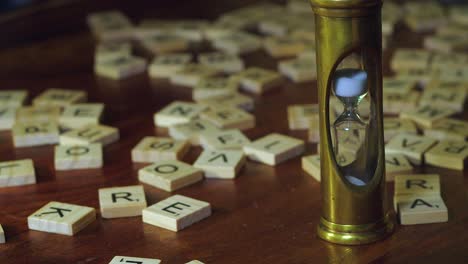 Antiguo-Reloj-De-Arena-De-Latón-Sobre-Una-Mesa-Con-Azulejos-De-Scrabble