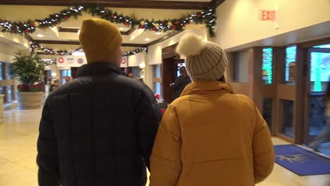 Man-and-woman-holding-hands-wearing-winter-jacket-coat-clothes-inside-mall-with-christmas-holiday-decorations-hanging-on-the-walls