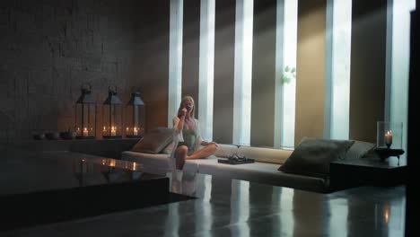 Woman-sitting-in-luxury-modern-spa-drinking-tea-with-light-rays-from-windows