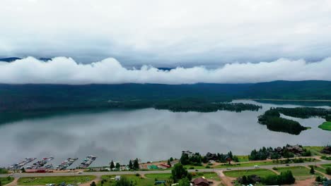 Beautiful-Shadow-Mountain-Reservoir-with-Low-Elevation-Clouds-on-an-Overcast-Summer-Day-in-Grand-Lake-Colorado-with-Cars-Driving-on-Highway-Road-Along-the-Shoreline
