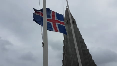 Bandera-Nacional-De-Islandia-Ondeando-Sobre-Un-Fuerte-Viento-Tormentoso-Frente-A-La-Iglesia-Hallgrimskirkja-En-El-Centro-De-Reykjavik