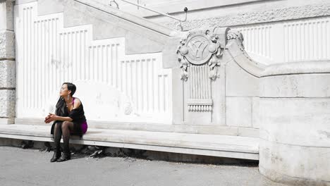 Tanned-asian-model-sitting-alone-on-stone-bench-of-historic-building-in-purple-and-black-clothes