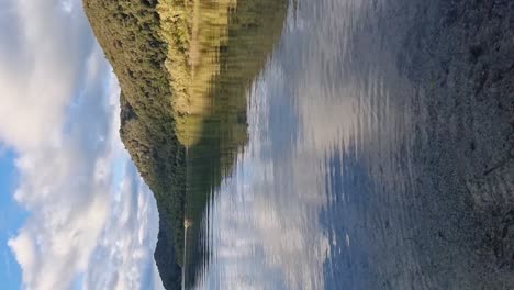 Vista-Vertical-Del-Lago-Azul-En-La-Orilla-Del-Lago-Que-Muestra-El-Reflejo-De-Las-Montañas-Y-Colinas-Cubiertas-De-Helechos-En-Rotorua,-Nueva-Zelanda