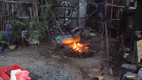 Old-blue-gas-cylinder-rolling-away-from-danger-of-burning-hot-fire