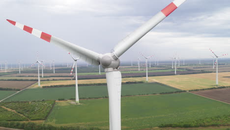 Luftaufnahme-Einer-Rotierenden-Windturbine-Vor-Dem-Hintergrund-Mehrerer-Turbinen-Auf-Flachem,-Offenem-Ackerland