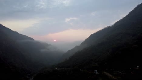Sunset-over-misty-mountains-with-a-glimpse-of-a-winding-road,-serene-evening