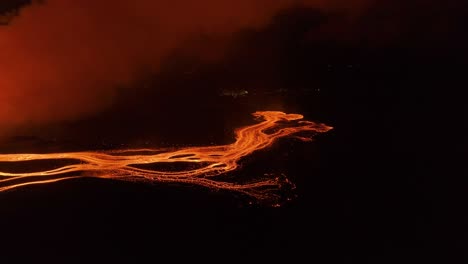 Branching-lava-stream-glowing-orange-in-night-time-scenery,-aerial