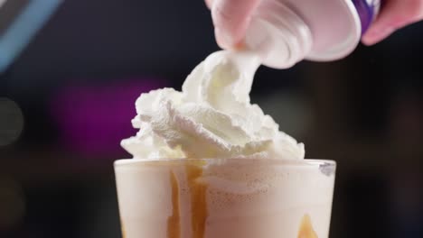 Spraying-whipped-cream-over-a-vanilla-milkshake-side-view-close-up
