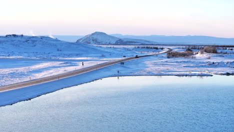 Winter-road-winding-through-snowy-Myvatn-volcanic-landscape-at-dusk,-with-a-calm-lake-and-soft-light