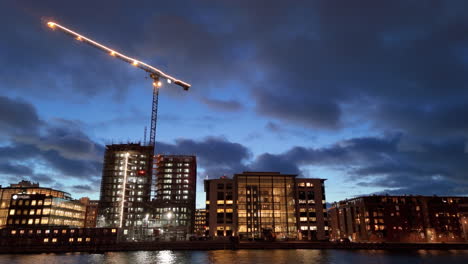 Illuminated-crane-and-buildings-at-construction-site-on-Malmo-waterfront,-drone