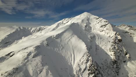 Sunlit-snowy-Lespezi-Peak-under-clear-blue-skies,-showcasing-winter's-majesty,-aerial-view