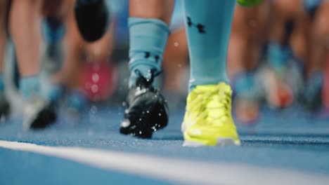 close-up-of-legs-of-several-female-hockey-players-as-they-run-across-wet-blue-grass-field-for-warm-up-in-slow-motion