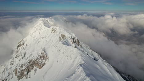 Snow-capped-Piatra-Craiului-Mountains-peak-rising-above-clouds,-aerial-shot,-serene-nature