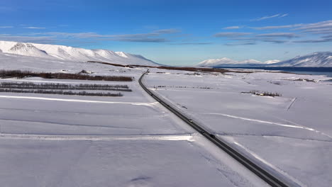 Luftaufnahme-Von-Autos,-Die-An-Einem-Sonnigen-Wintertag-über-Eine-Fjordstraße-In-Akureyri,-Island-Fahren