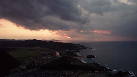 Espectacular-Puesta-De-Sol-Aérea-Sobre-El-Mar-De-Japón,-Playa,-Montaña,-Horizonte,-Nubes-De-Drones-Se-Mueven-En-Cámara-Lenta-Sobre-Kyotango