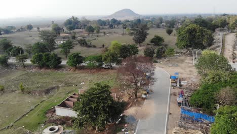 Toma-Aérea-De-Un-Pueblo-En-Jharkhand-Con-Carretera-Asfaltada-Y-Vegetación-Verde-Y-Montaña-En-La-India