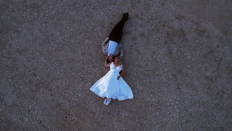 Top-Down-Aerial-View-of-Romantic-Newlywed-Couple-Lying-on-Dry-Ground-of-Nevada-Desert