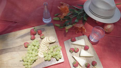 top-down-of-vegetarian-appetiser-vegan-cheese-and-fruit-strawberry-grape-fruit-on-red-tablecloth-outdoor-picnic-concept