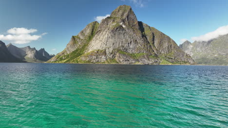 drone-flying-low-over-aqua-blue-water-towards-a-large-mountain-in-Lofoten,-Norway