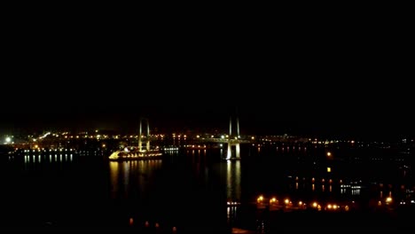 Nachtansicht-Einer-Brücke-über-Dem-Wasser-Mit-Den-Lichtern-Der-Stadt,-Die-Sich-Auf-Der-Oberfläche-Spiegeln,-Ruhige-Und-Heitere-Szene