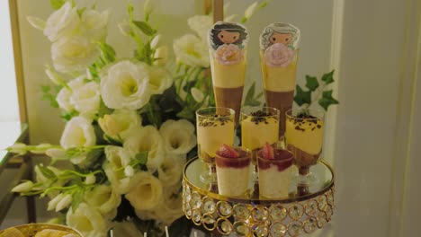 Close-up-shot-showing-a-cake-stand-with-multiple-dessert-glasses,-white-flower-decorations-in-the-background