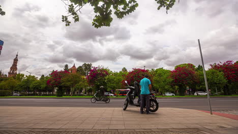Motor-Cyclist-pausing-on-vibrant-Seville-street-with-blooming-trees,-timelapse