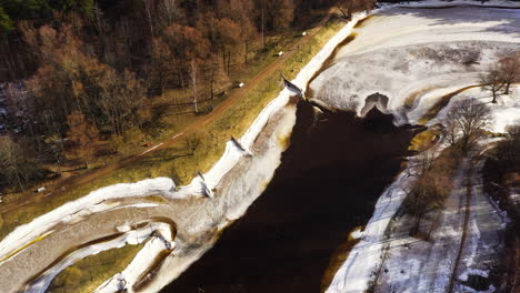 Der-Fluss-Gauja-In-Valmiera-Ist-Im-Winter-Zugefroren,-Verschneites-Flussufer-Und-Wald
