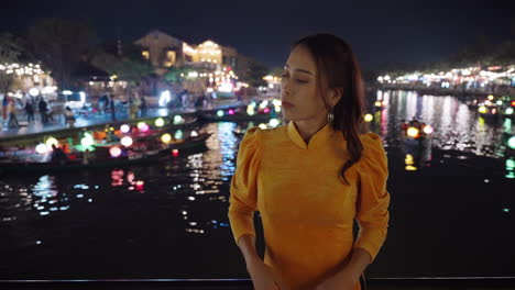 Mujer-Vestida-De-Amarillo-Ao-Dai-Con-Vistas-Al-Río-Iluminado-Por-Linternas-En-Hoi-An-Por-La-Noche,-Reflejando-La-Esencia-Cultural