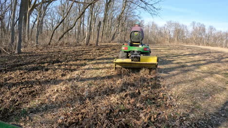 POV-Siguiendo-A-Un-Hombre-En-Un-Tractor-Utilitario-Remolcando-Un-Motocultor-Para-Aflojar-La-Tierra-En-Una-Parcela-De-Alimento-Para-Ciervos-Entre-La-Madera-Y-El-Campo-A-Principios-De-La-Primavera