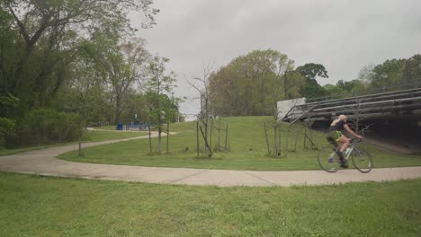 A-slow-motion-view-of-a-young-female-cyclist-rides-her-bike-on-Bay-Area-Hike-and-Bike-Trail-along-Horsepen-Bayou-on-an-overcast-day-in-Clear-Lake,-Houston,-Texas