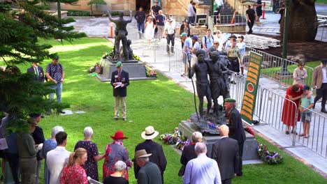 Veterans-and-families-gathered-at-Brisbane's-Anzac-Square,-encircling-the-bronze-sculpture-of-the-South-West-Pacific-Campaign-during-the-day,-paying-homage-to-those-who-served