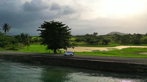 Siguiendo-Un-Coche-En-La-Costa-En-Un-Día-Soleado,-Rodeado-Por-Un-Magnífico-Paisaje-Verde-En-Santo-Tomé,-África