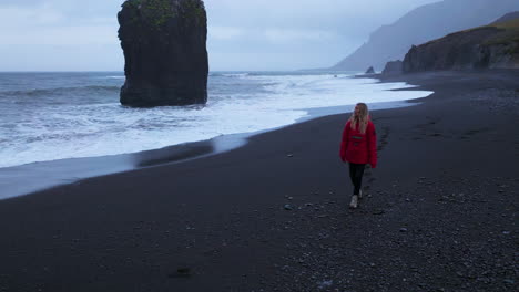 Turista-Con-Chaqueta-Roja-Caminando-Sobre-Arena-Negra-En-La-Playa-De-Laekjavik-En-Islandia