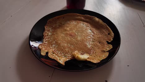 Clumsy-shaped-pancake-on-a-black-plate-on-white-table