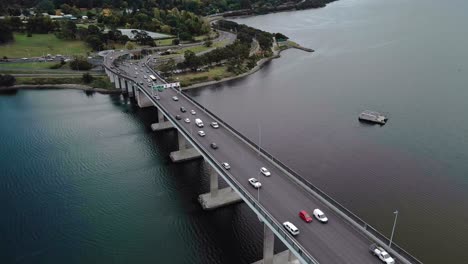 Aerial-view-of-vehicles-running-on-a-bridge-over-a-calm-river