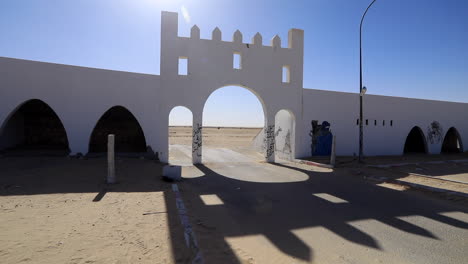 Sunlit-ancient-Sahara-gate-with-blue-sky,-sand-on-ground,-graffiti-on-walls,-shadow-patterns