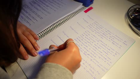 Nahaufnahme-Der-Hände-Des-Mädchens-Mit-Ringen,-Während-Sie-Spät-In-Der-Nacht-Weiterhin-Notizen-Auf-Millimeterpapier-Mit-Blauem-Stift-Schreibt