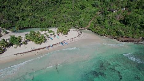 Aerial-flying-backwards-from-tourists-enjoying-Rincon-beach-on-sunny-day,-Caribbean