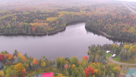 Aerial-shot-of-a-stunning-Lake-with-cottages-and-fall-colored-trees-around-it